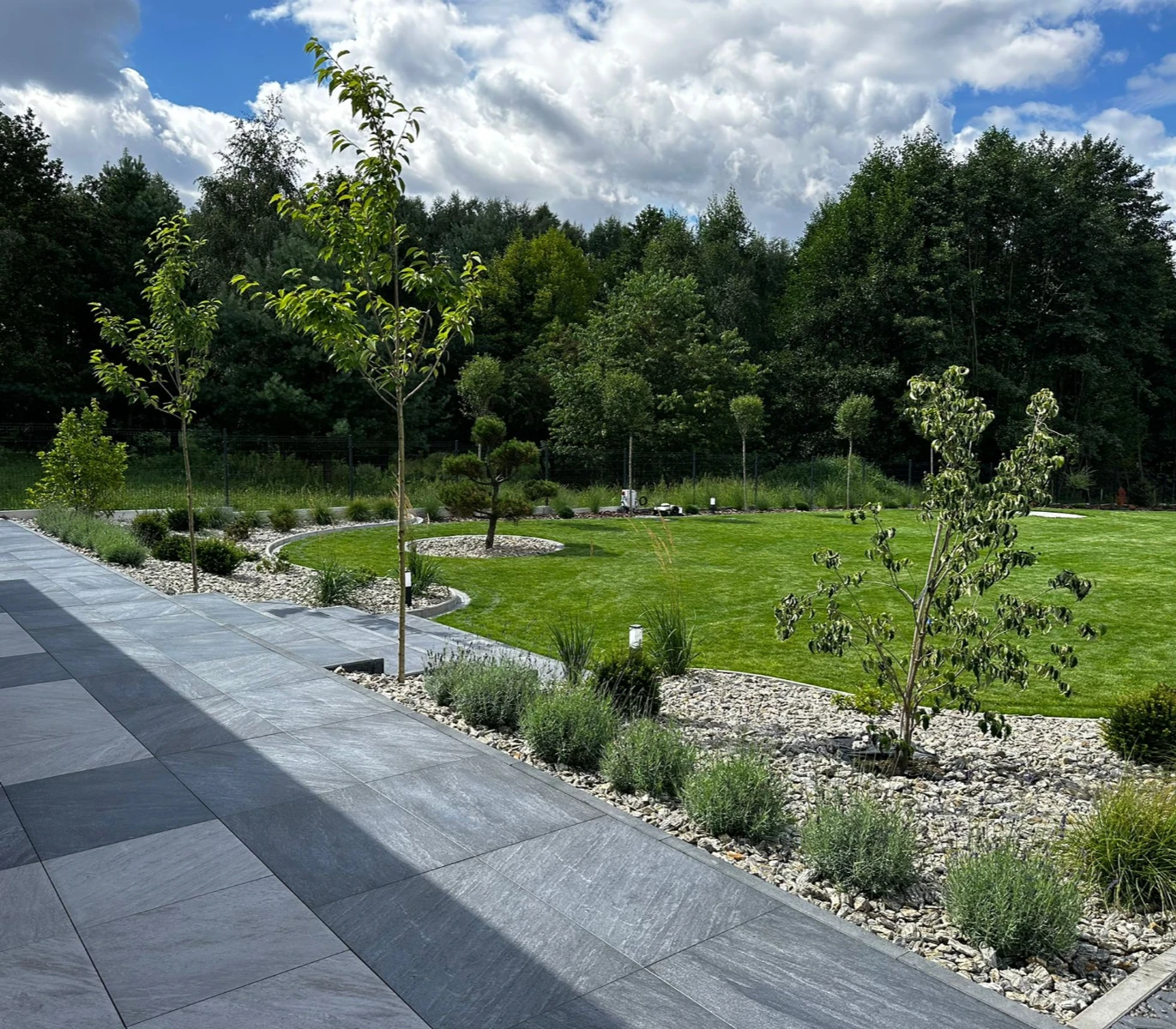 Taras z płyt gresowych z obrzeżem z kostki wokół trawnika i rabatami roślinnymi