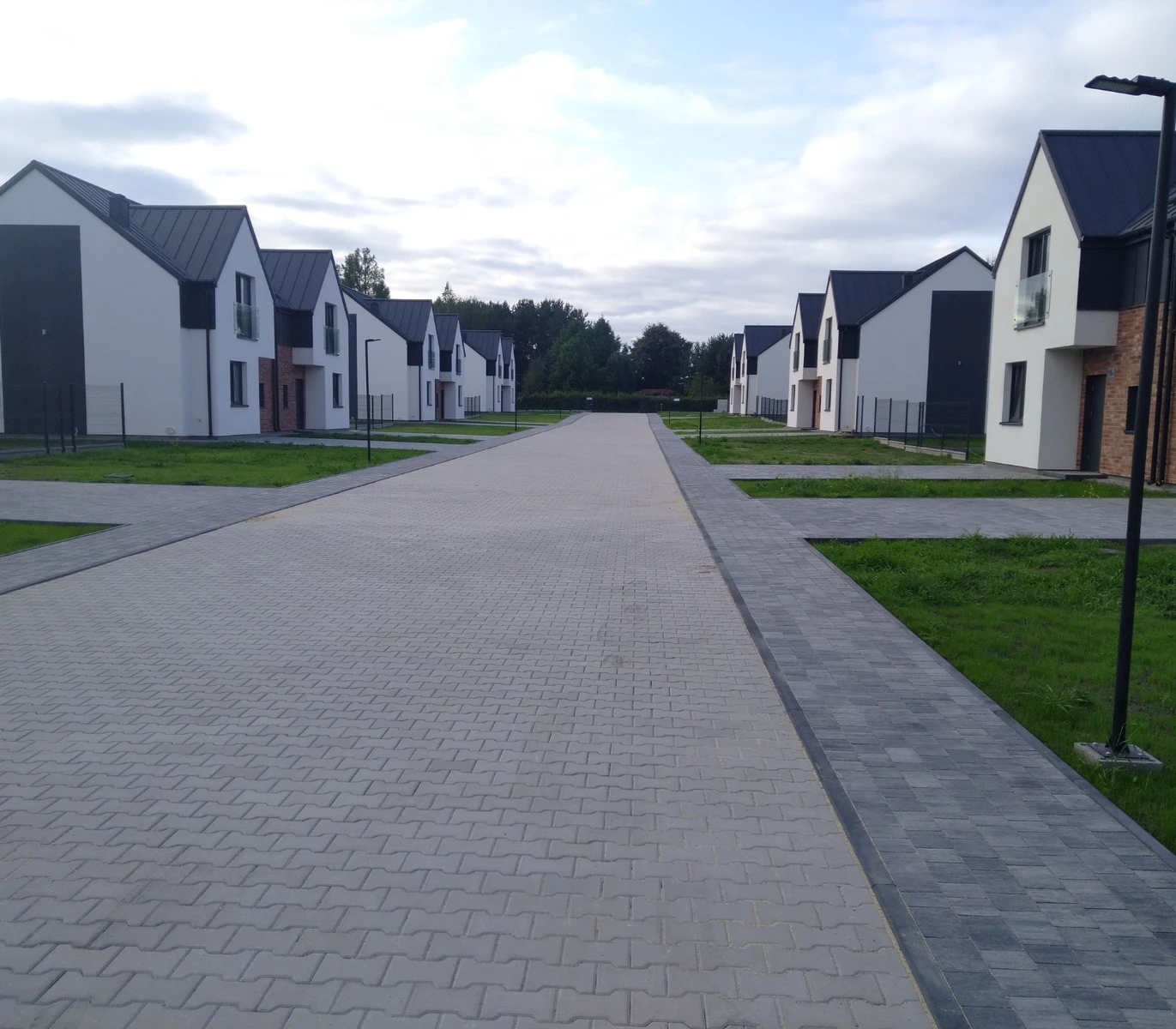 Wybrukowana droga dojazdowa pomiędzy nowymi domami jednorodzinnymi