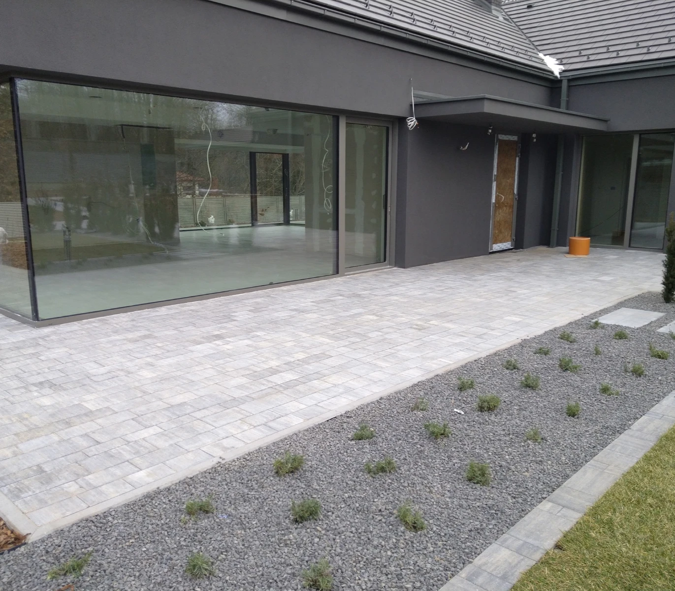 Tarasy z szarej kostki brukowej wzbogacone żwirową opaską przy nowoczesnym domu