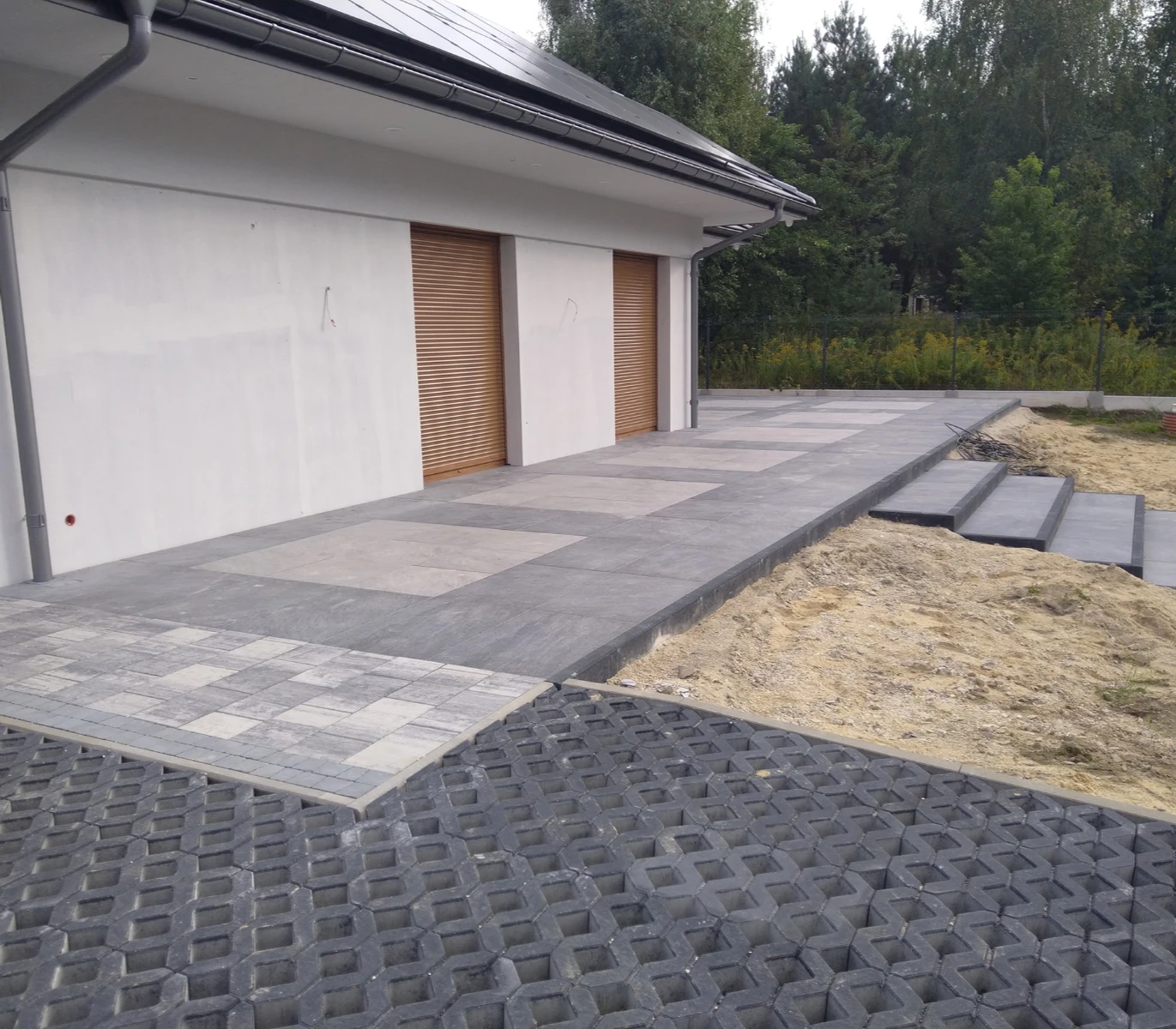 Tarasy z dużych szarych płyt gresowych przy białej elewacji domu