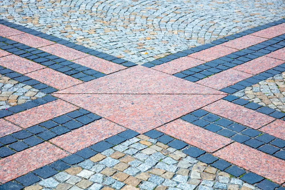 Dekoracyjna nawierzchnia kostki brukowej w odcieniach szarości, beżu i czerwieni ułożona w geometryczny wzór