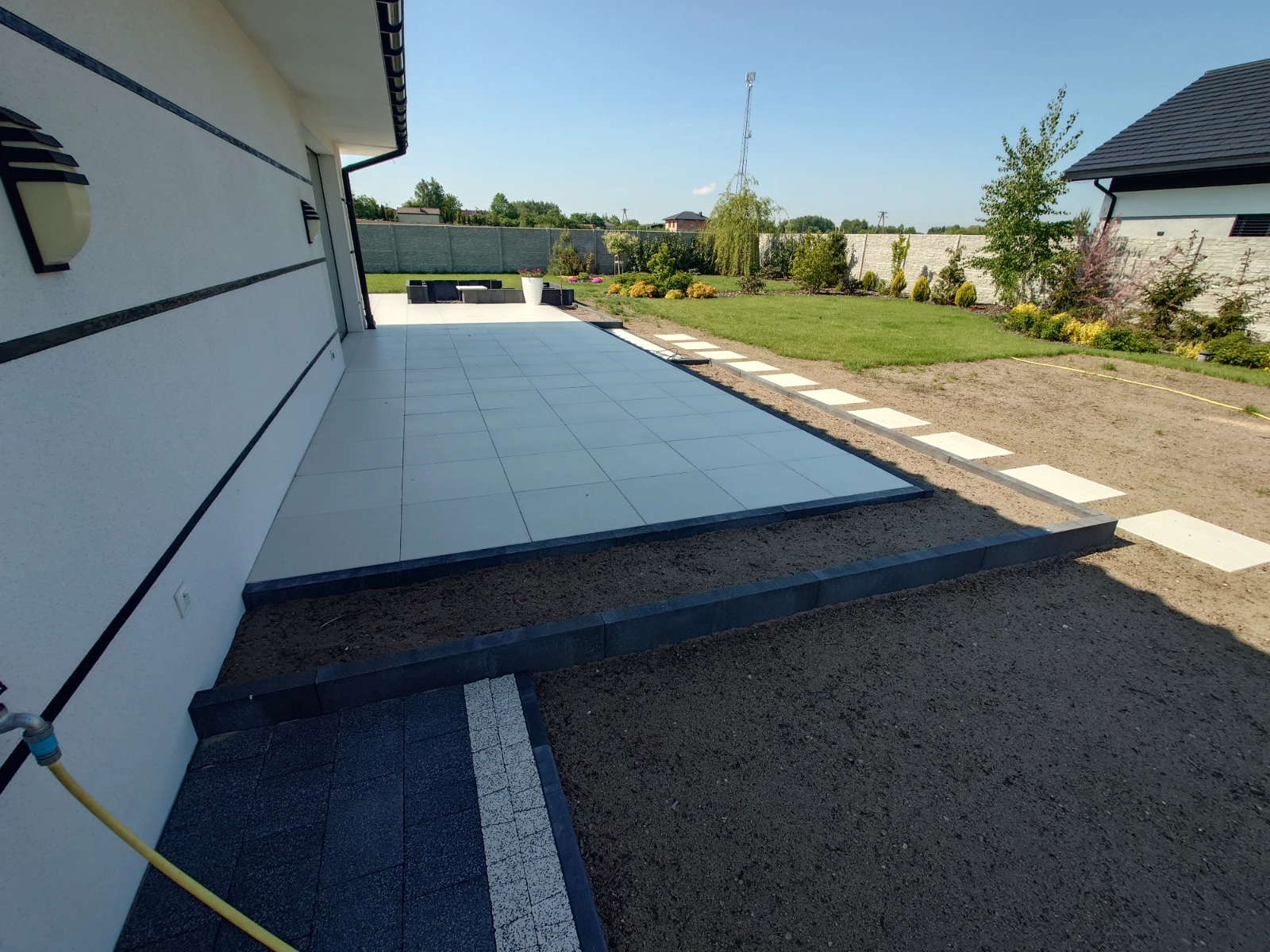 Taras z dużych płyt gresowych ułożony wokół domu z betonową opaską i ścieżką z płyt prowadzącą do ogrodu