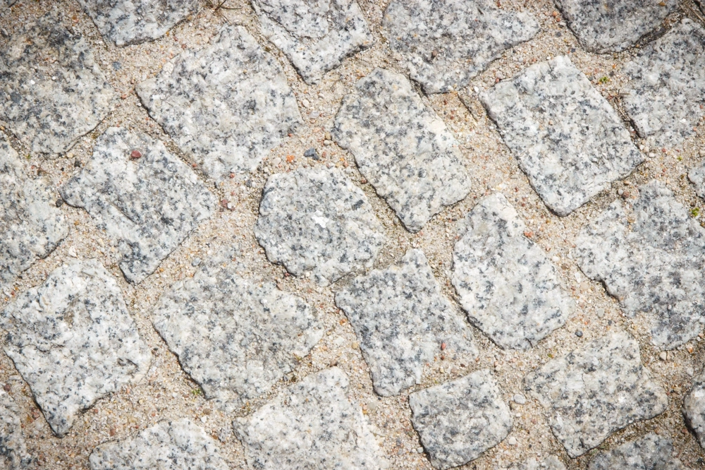 Ułożona na podjeździe kostka granitowa w nieregularny wzór na jasnym podłożu z piasku